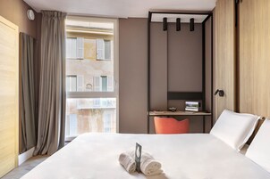 Een hotelkamer met een groot bed, een bureau met een computer, een zithoekje en uitzicht op de stad.