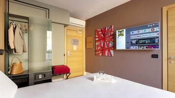 Ein Hotelzimmer mit Bett, Kleiderschrank, einer Garderobe, einem roten Koffer, einem an der Wand befestigten Fernseher, der Streaming-Dienste anzeigt, und einer Tür mit Holzpaneelen.