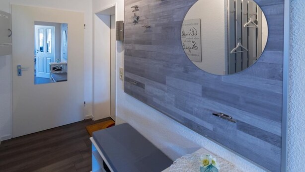 Ein modernes Badezimmer mit Wandverkleidung aus grauem Holz, einem großen Spiegel und einem weißen Waschtisch mit einer dekorativen Vase.