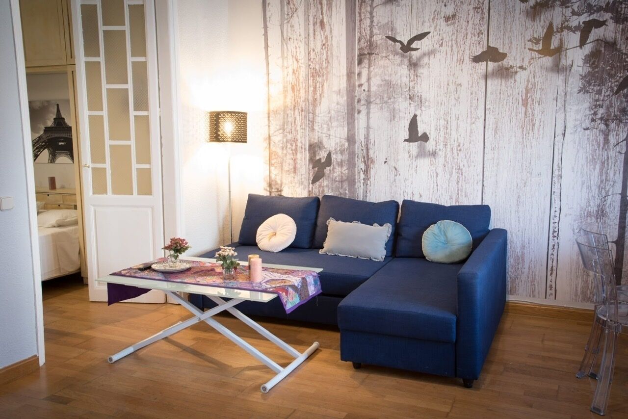 A living room with a blue sofa, a glass coffee table, and a wall with a rustic design.