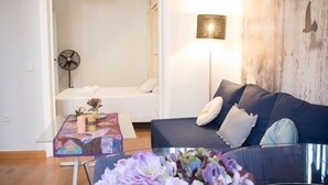 Un salon moderne avec un canapé, une table ornée d’un vase de fleurs, un ventilateur et un luminaire fixé au mur.