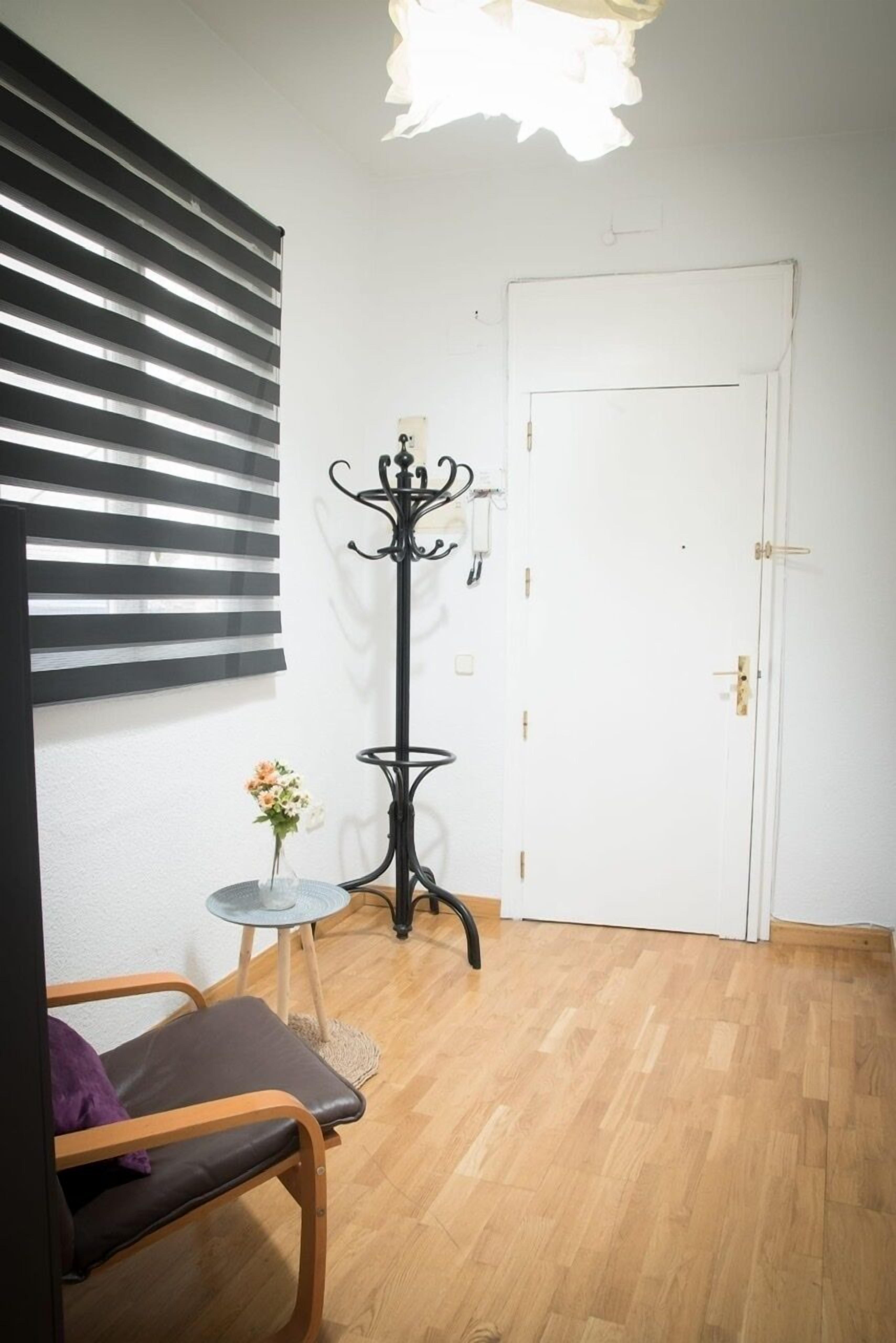 A room with a wooden floor, a white door, a black metal coat stand, and a small round table with a vase of flowers.