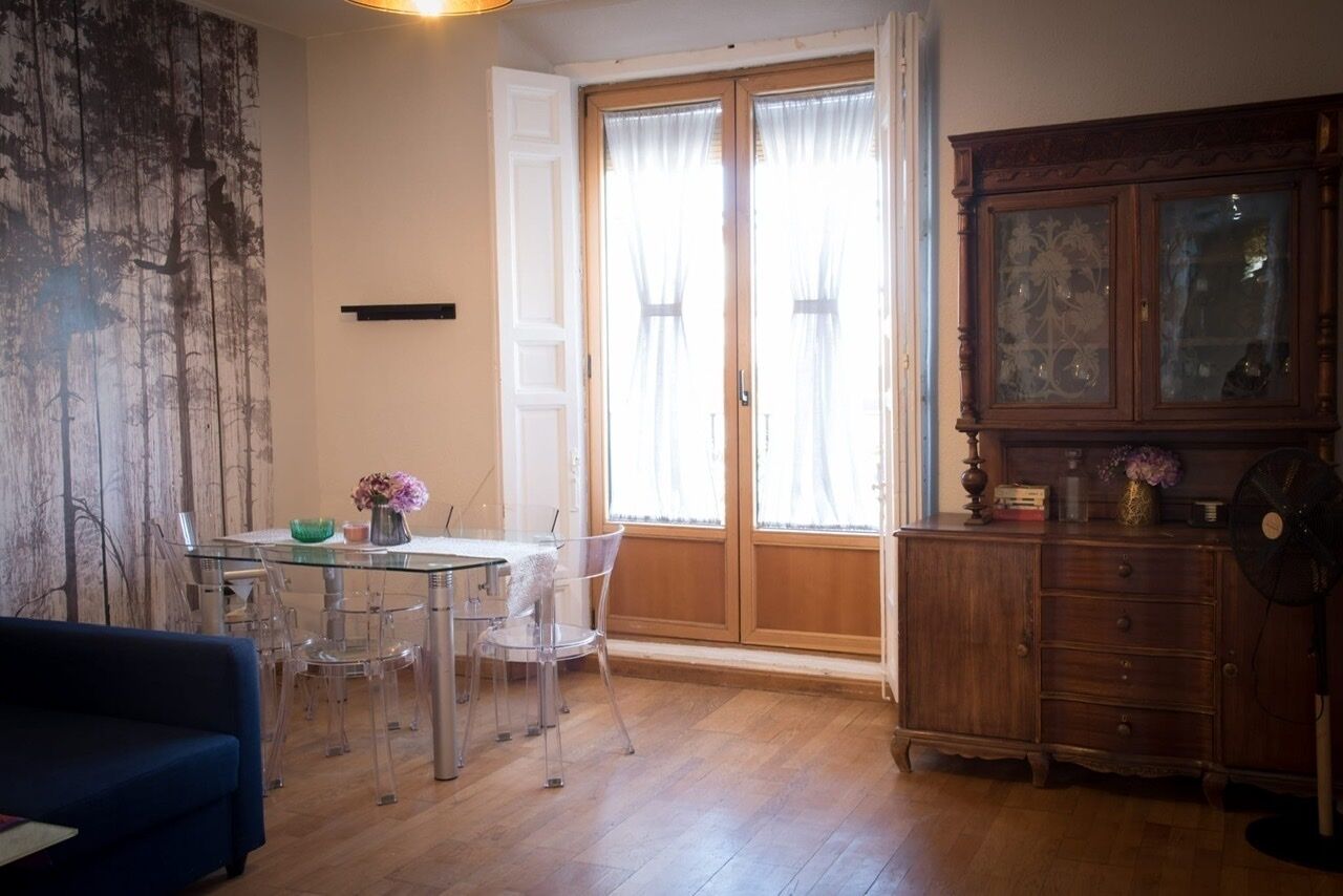 Une pièce avec une table à manger en verre, des chaises transparentes, un canapé bleu, un meuble en bois et une grande fenêtre avec des rideaux.