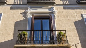 Fachada de edificio con balcón, barandilla de hierro forjado y plantas en macetas.