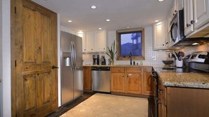 Une cuisine avec des meubles en bois, des appareils électroménagers en acier inoxydable et une vue sur un immeuble par la fenêtre.