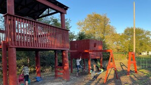 Une aire de jeux dotée d’une structure en bois, comprenant un toboggan et des balançoires.