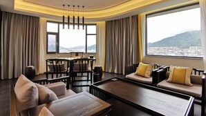 A modern hotel room with a curved ceiling, a dining area, a sofa set, and large windows offering a city view. - Longling Hotel (Longling)