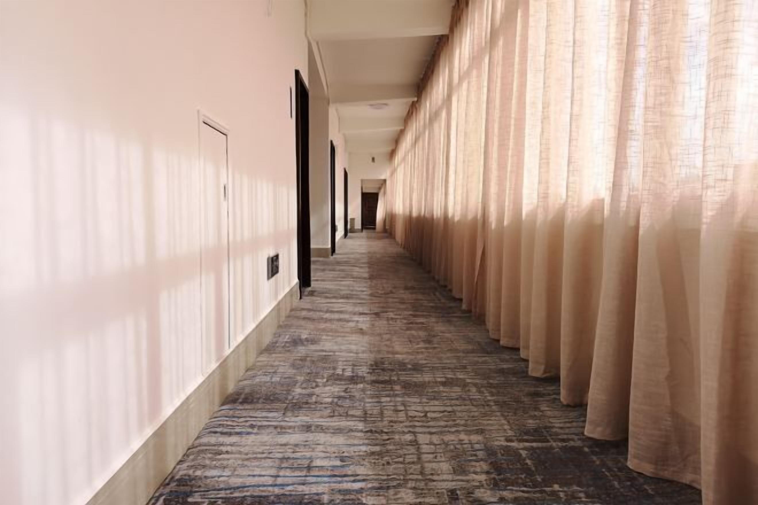 A hotel hallway with a carpeted floor, beige walls, and curtains on one side.