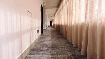 A hotel hallway with a carpeted floor, beige walls, and curtains on one side.