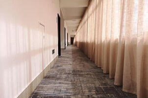 Un pasillo de hotel con piso alfombrado, paredes color beige y cortinas a un lado.
