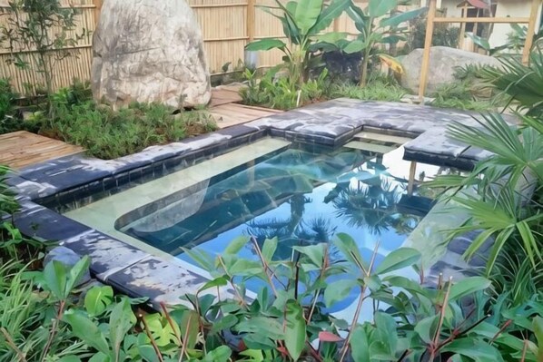 A hot tub surrounded by greenery and rocks.