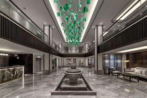 A spacious lobby with a central fountain, a reception desk, and a seating area. - Longling Hotel (Longling)