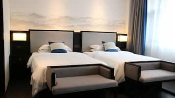 Quarto de hotel com duas camas, mesas de cabeceira e um banco.