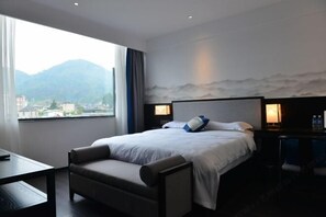 A hotel room with a bed, a desk, a chair, and a view of mountains.