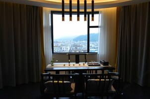 A room with a large window, a table, chairs, and a vase with flowers.
