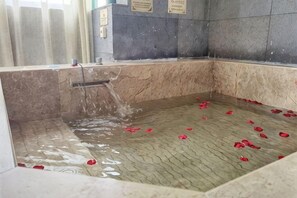 A marble-floored bathtub with rose petals scattered on the floor.