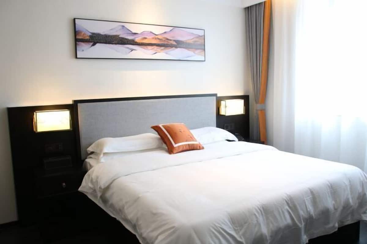 Et hotelværelse med en seng, et natbord, et vægmonteret fjernsyn og et billede over sengen.