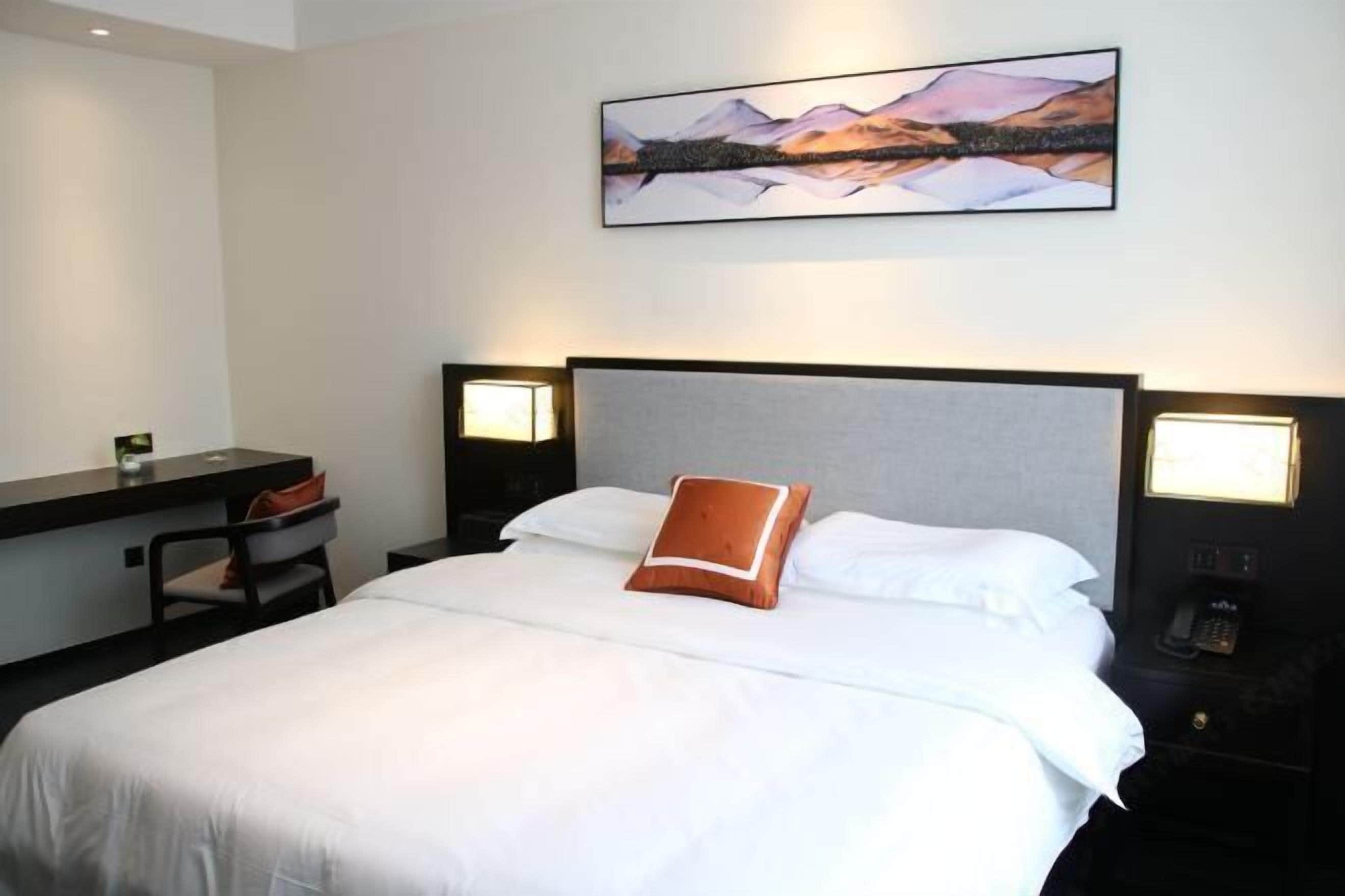 Habitación de hotel con una cama grande, un escritorio y una silla. Hay un cuadro en la pared sobre la cama.