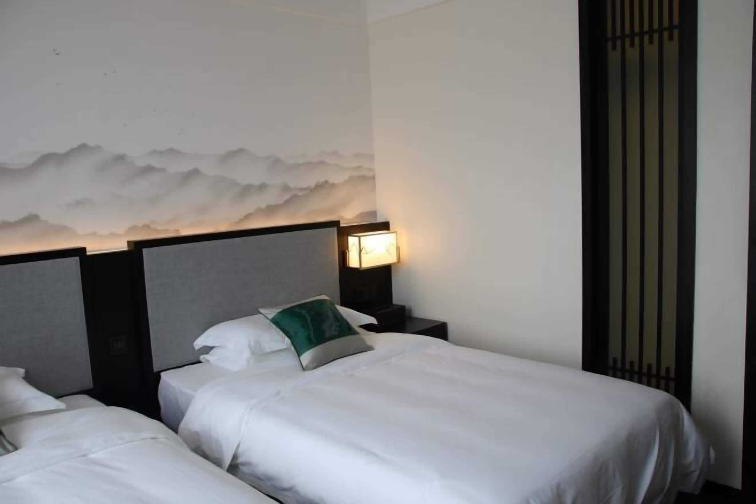 Camera d'albergo con due letti, un affresco, un comodino con lampada e una finestra in stile tradizionale.