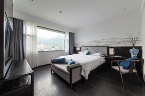 A modern hotel room with a large bed, a desk, and a view of a cityscape through the window. - Longling Hotel (Baoshan)