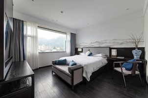 Habitación de hotel moderna con una cama grande, un escritorio y vistas a un paisaje urbano a través de la ventana.