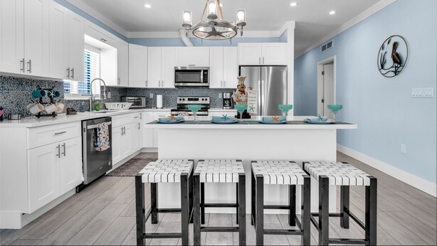 Una cocina moderna con armarios blancos, una isla central con taburetes de bar, electrodomésticos de acero inoxidable y una obra de arte con pájaros en la pared.