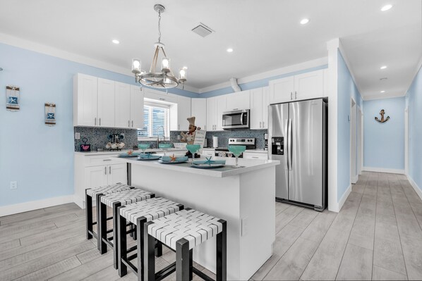A modern kitchen with white cabinets, a central island, bar stools, stainless steel appliances, and decorative elements.
