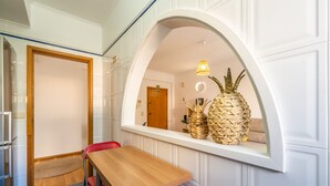 A dining area with a wooden table and chairs, a small rug, and a window with wicker baskets. - Apartment ElDoMar (Funchal)
