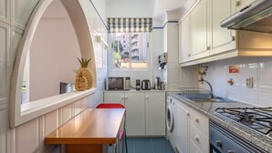 A compact kitchen with a wooden table, a washing machine, a microwave, and a gas stove. - Apartment ElDoMar (Funchal)