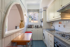 Compact kitchen with a table, chair, and window offering a view of the outside. Equipped with a microwave, coffee maker, and washing machine, as well as a gas stove and range hood.