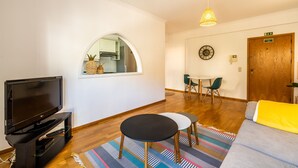 A living room with a television, a round table, a sofa, and a window overlooking a kitchen. - Apartment ElDoMar (Funchal)