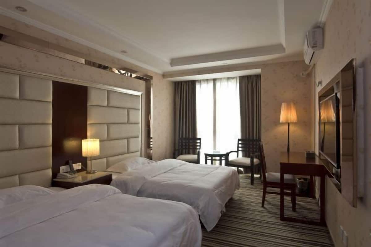 Quarto de hotel com duas camas, uma mesa, uma cadeira, uma televisão e janela com cortinas.