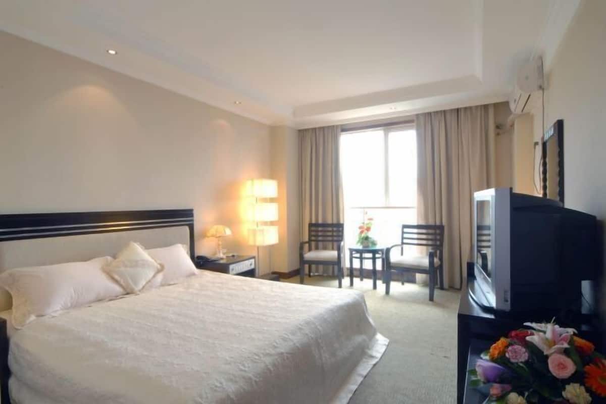 Quarto de hotel com uma cama grande, uma escrivaninha com luminária, televisão e uma pequena mesa com flores.