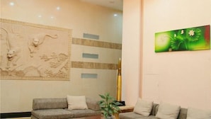 A lobby with a sofa, a painting of flowers, and a decorative wall with a relief sculpture.