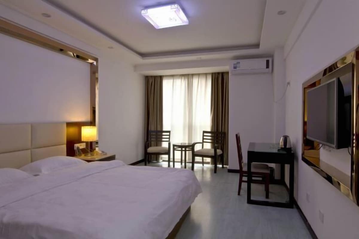 A hotel room with a bed, a desk, a chair, a TV, and a window with curtains.