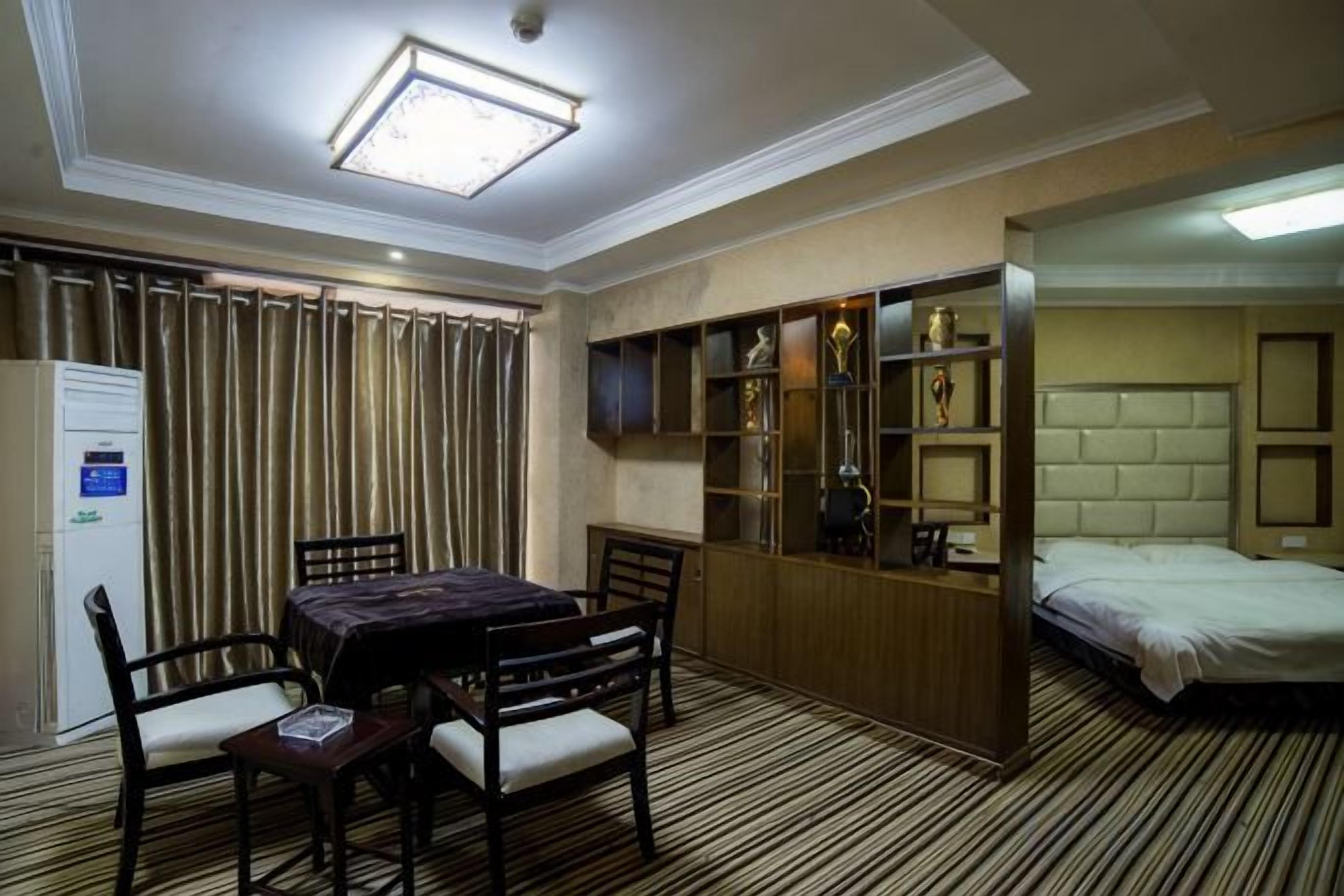 A hotel room with a dining table, chairs, a bed, a wardrobe, and a built-in shelf unit.