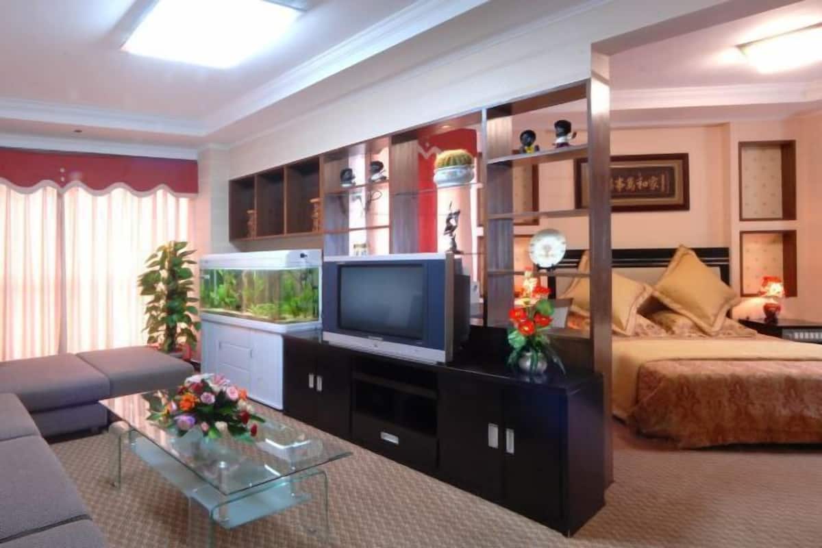 Uma sala de estar com sofá, mesa de centro de vidro, televisão, aquário e cama com almofadas.