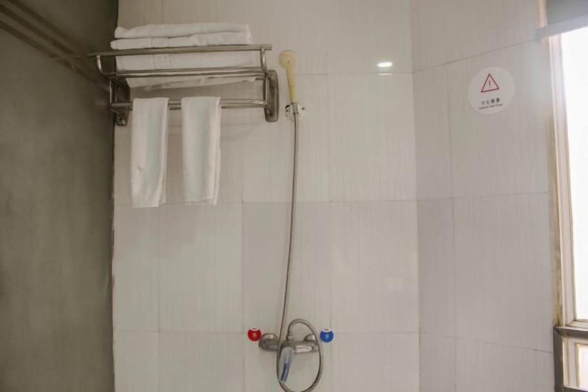A bathroom with a shower, a towel rack with folded towels, and a warning sign on the wall.