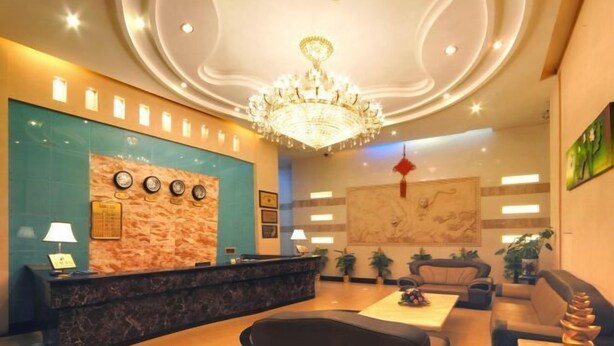 A hotel lobby with a reception desk, seating area, chandelier, and decorative wall elements.