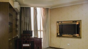 A hotel room with a desk, chair, air conditioning unit, and a television mounted on the wall.