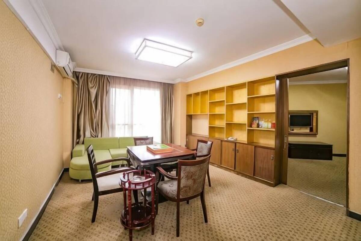 Quarto de hotel com mesa de jantar, cadeiras, sofá, televisão e estante de livros.