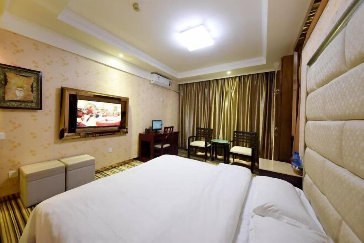 Quarto de hotel com cama, escrivaninha, cadeira, televisão e janela com cortinas.