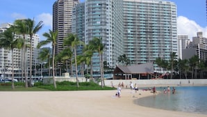 A beachfront hotel with multiple high-rise buildings, palm trees, and a sandy beach with people enjoying the water. - Resort Style with Hula Show, Fireworks and even Tiki Torches! (Honolulu)