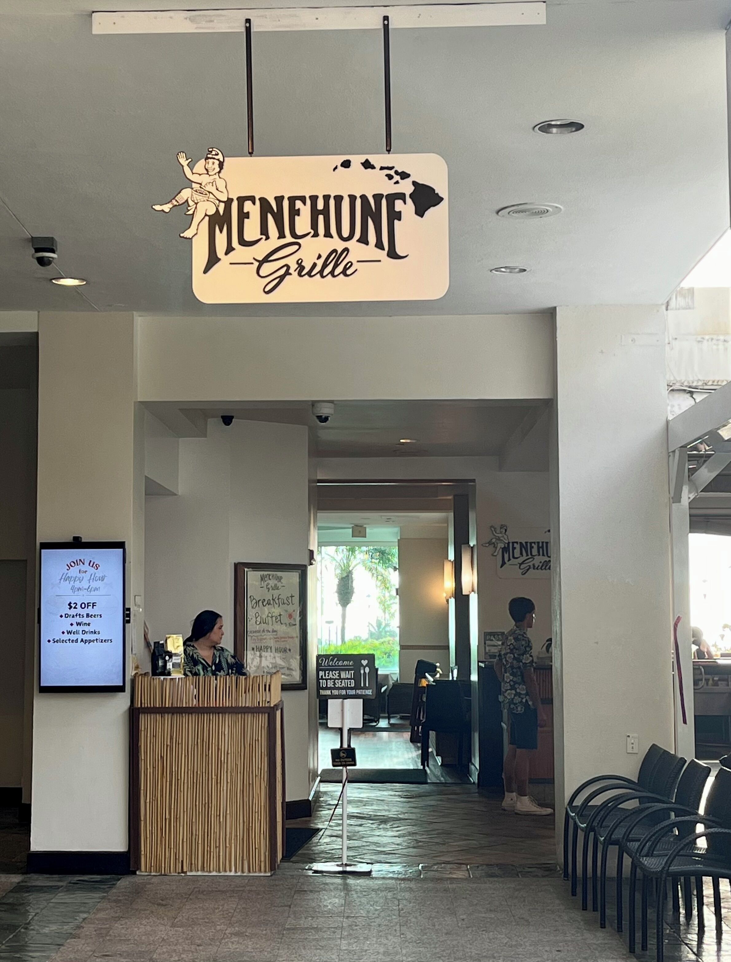 A restaurant interior with a sign reading "Menehune Grille" and a reception desk.