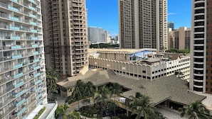 A high-rise residential building with multiple balconies, a rooftop pool, and surrounding palm trees. - Resort Style with Hula Show, Fireworks and even Tiki Torches! (Honolulu)