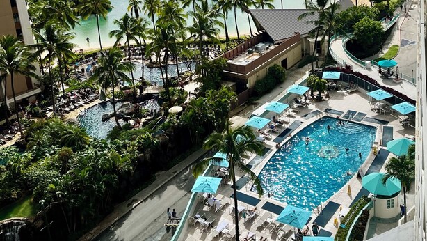 A resort with a large pool, palm trees, and a beach view. - Resort Style with Hula Show, Fireworks and even Tiki Torches! (Honolulu)