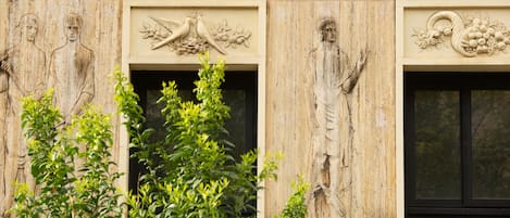 A building facade with carved reliefs of human figures and birds, surrounded by greenery.