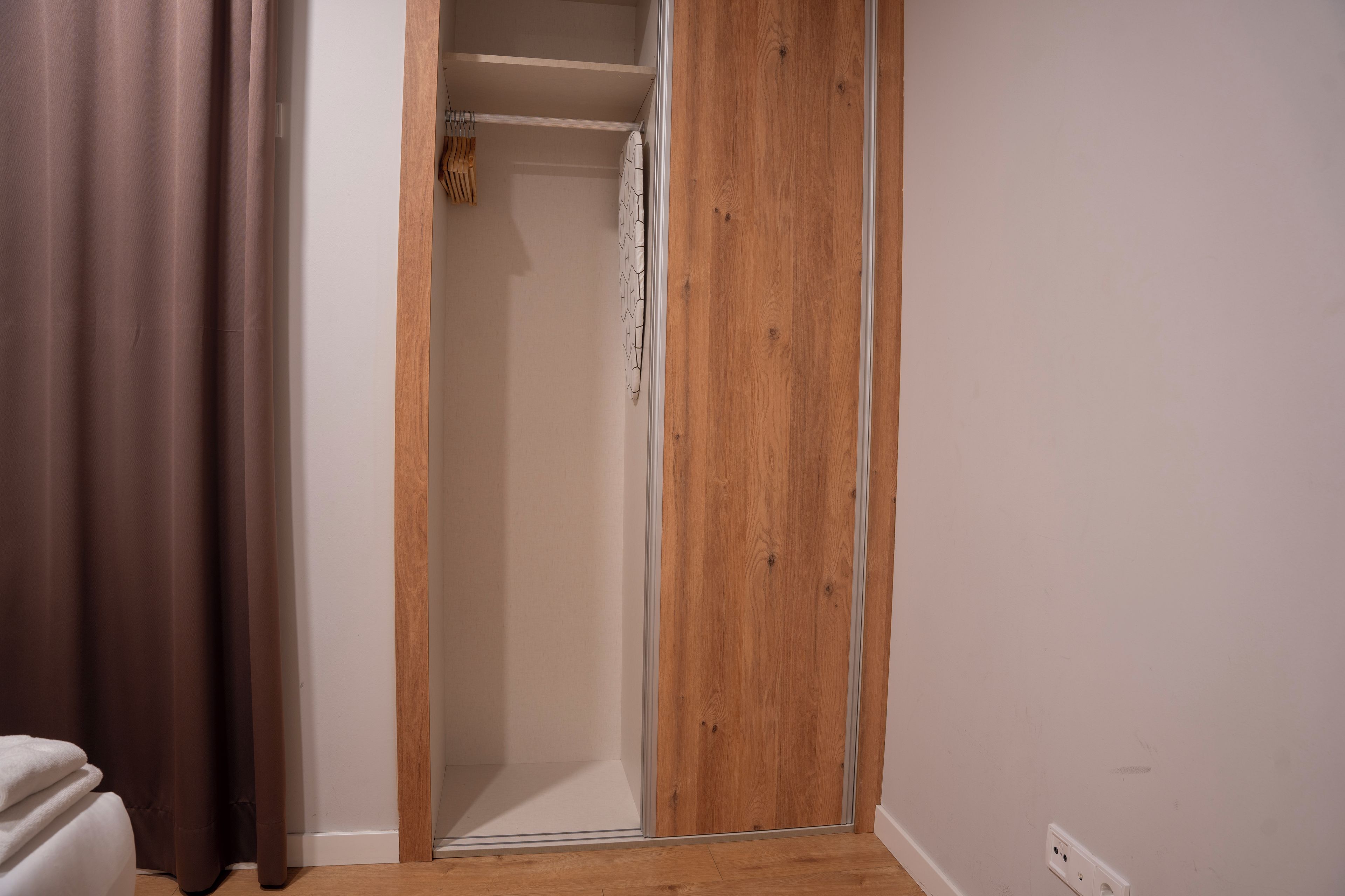 A room with a wooden door, a white wall, and a brown curtain.
