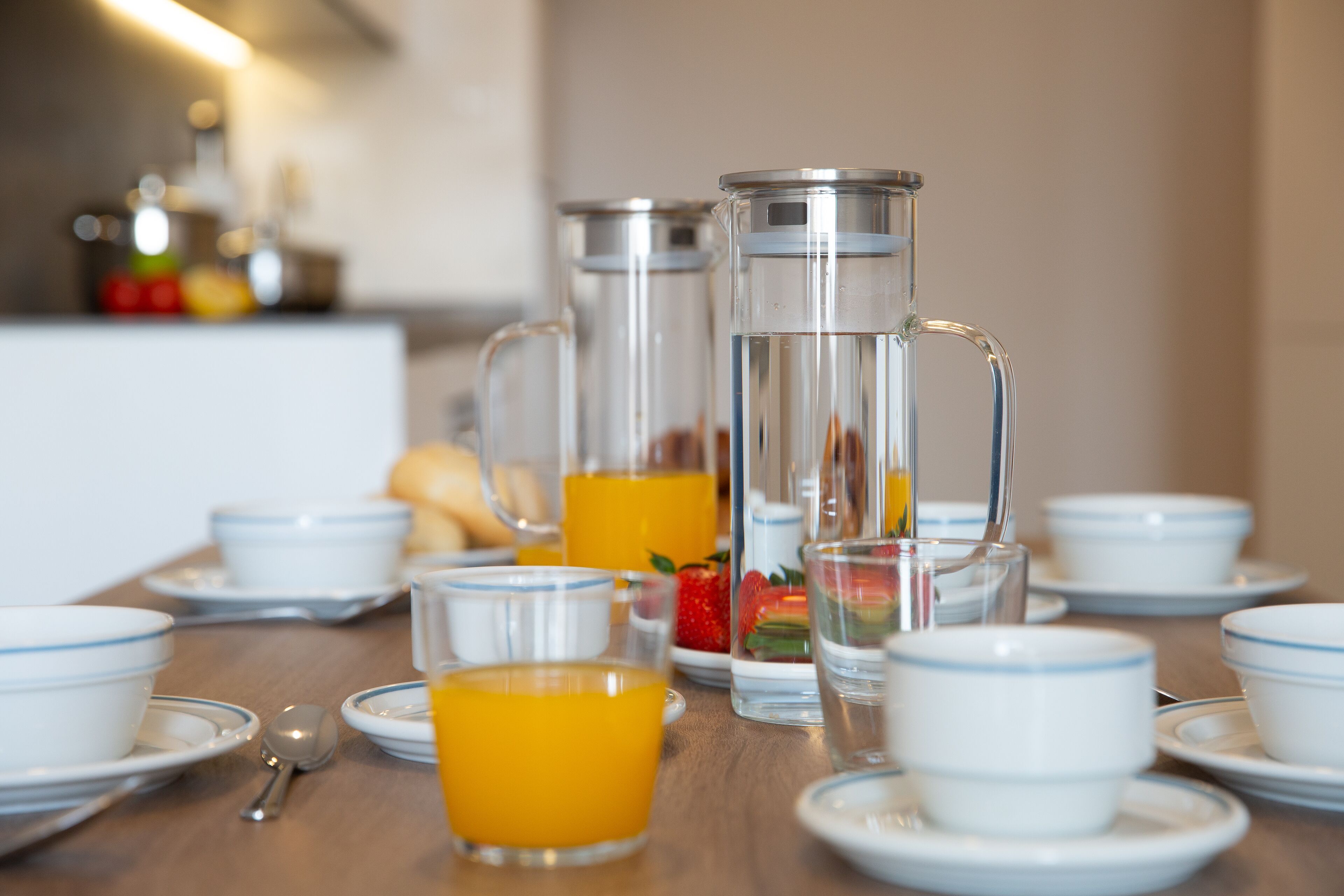A breakfast table set with white cups, saucers, a glass pitcher, and a glass of orange juice.
