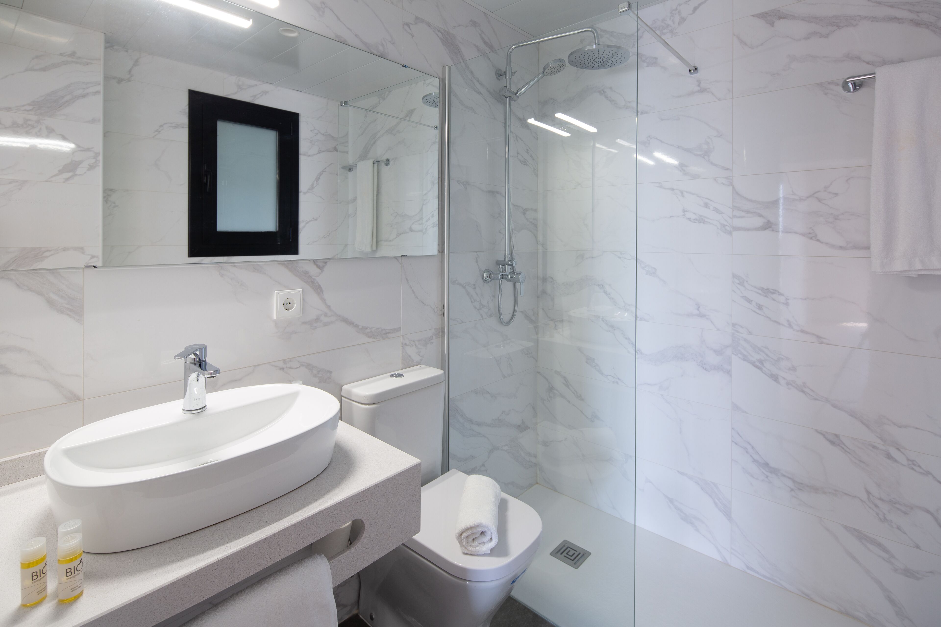 A modern bathroom with a large oval sink, a toilet, and a glass-enclosed shower.
